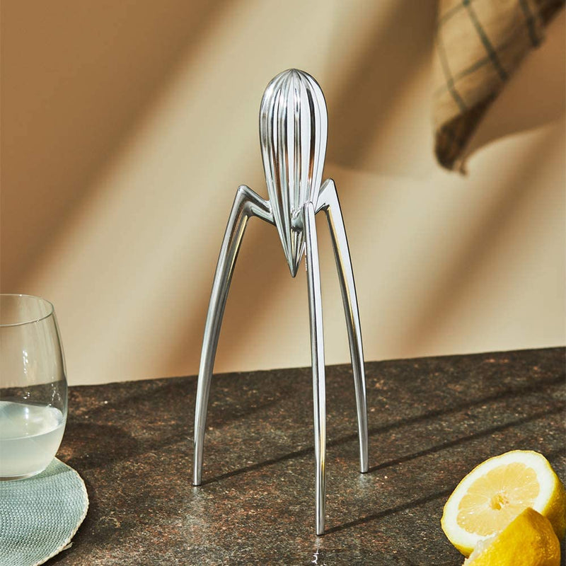 Alessi Juicy Salif citrus juicer in aluminium casting in a kitchen counter with a lemon cut in half and a glass with lemon juice