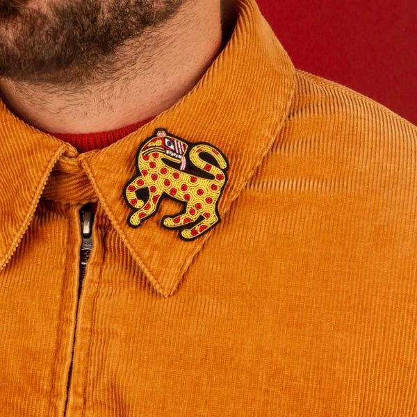 Leopard handmada brooch in yellow, red, purple and pink on the collar of an orange jacket. Designed by French company Macon et Lesquoy. Available at www.cuemars.com