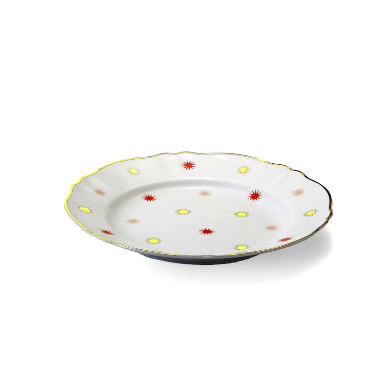 Porcelain dinner plate from Bitossi Home’s Abracadabra collection, showcasing a bold, multicolored starburst pattern with asymmetrical design elements and refined gold detailing around the rim.