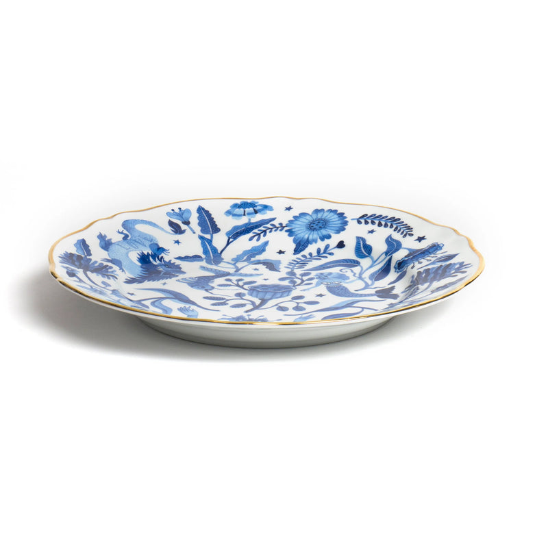 Decorative dinner plate from Bitossi Home's Fabula collection featuring intricate blue illustrations of a dragon, mermaid, birds, and floral motifs on a white background, with a scalloped edge and gold trim.
