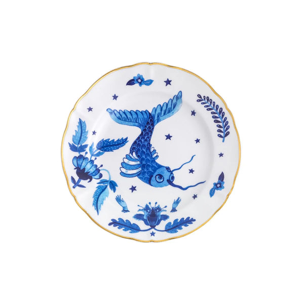 Fruit plate from Bitossi Home's Fabula collection featuring a whimsical blue fish surrounded by floral motifs and stars on a white background, with a scalloped edge and gold trim.
