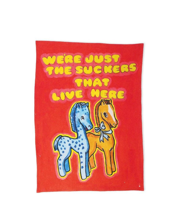 Colourful linen towel featuring two wooden horses and the typography We're just the suckers that live here, available at www.cuemars.com