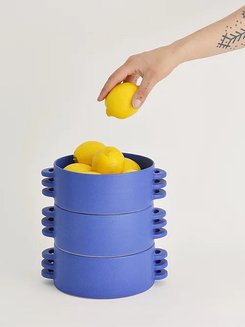three blue ceramic fruit bowls with lemons in them, each made with three horizontal handles made and painted by hand by ceramics by laura and a hand holding a lemon