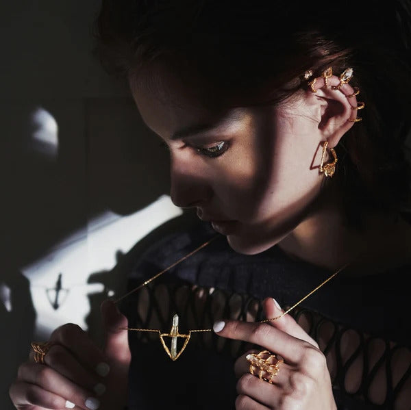 Woman wearing different triangle shaped jewellery pieces in gold plated and a transparent gemstone by Niza Huang, available at www.cuemars.com