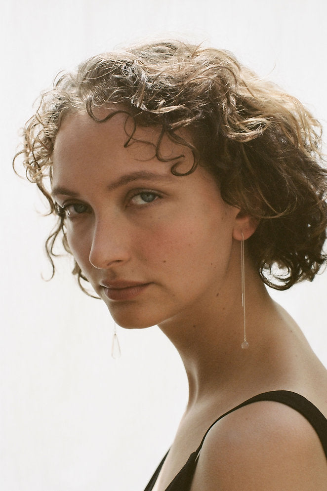 Model wearing a long delicate thread earring with a crystal rock sphere at the bottom