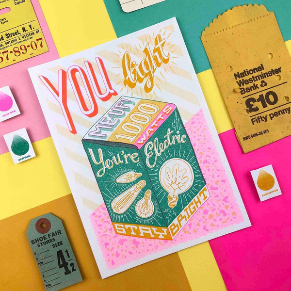 a greenm yellow, pink and orange light bulb box with the typography You Light Me Up - 1000 Watts - You're Electric - Stay Bright, by British illustrator Jacqueline Colley
