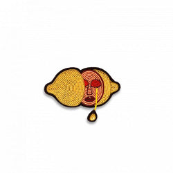 lemon cut in half hand-embroidered brooch in yellow, peach and red, showcasing a crying face whose tears are lemon juice. Designed by Macon et Lesquoy and available at www.cuemars.com