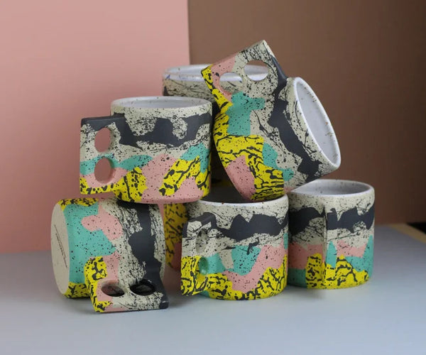 Colourful coffee mug with a geometrical handle with two holes for the fingers by Minx Factory, available at cuemars.com