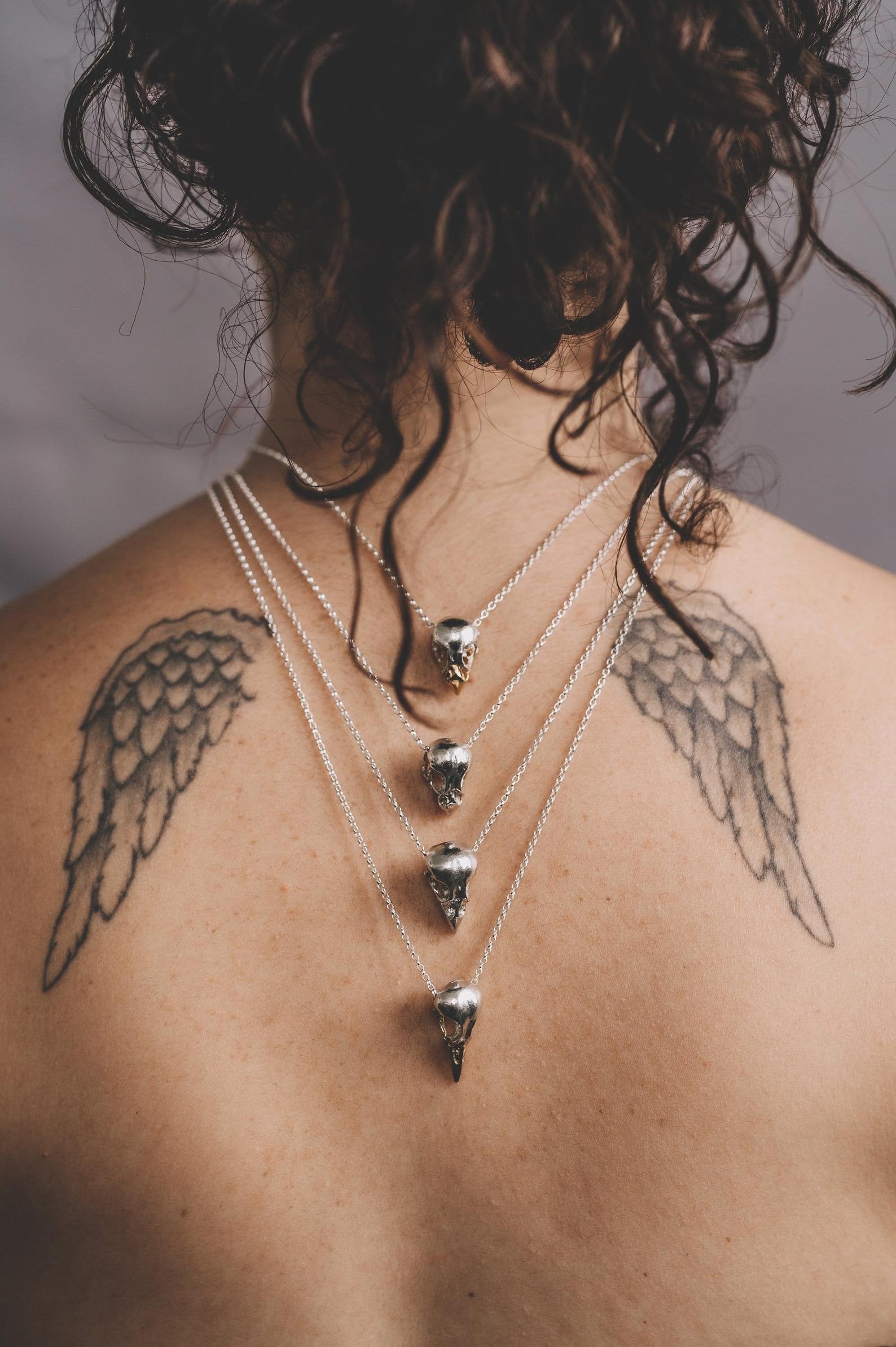 Details of several handmade bird skulls necklaces in sterling silver and a 24ct gold plated beak 