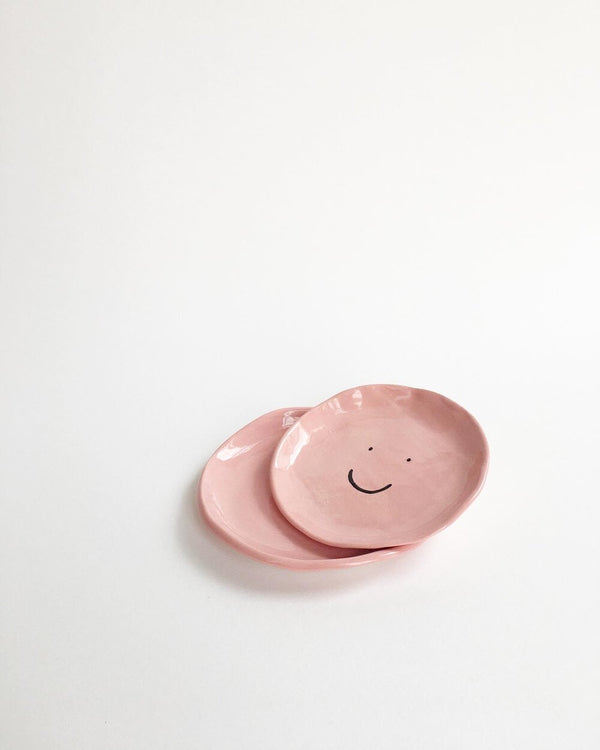 Pink ceramic dish with a black smiley face by illustrator Amy Victoria Marsh, available at www.cuemars.com